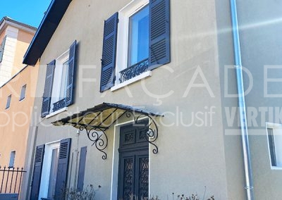 Façade de maison avec volets bleus et auvent décoratif.