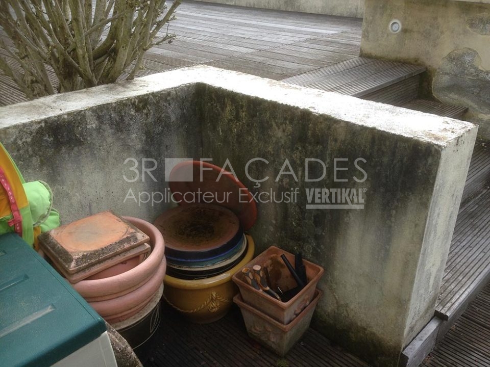 Pots de fleurs et outils rangés contre un mur en béton.