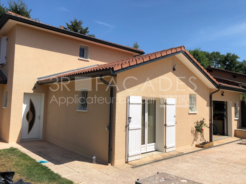 Maison beige avec portes et fenêtres blanches, toiture rouge.