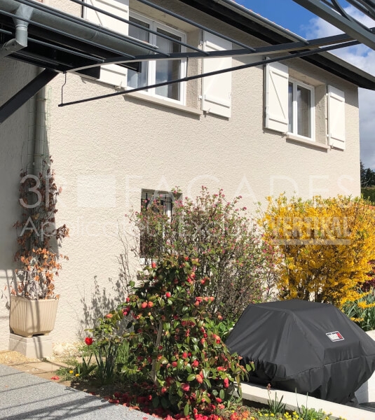 Maison avec jardin fleuri et barbecue couvert.