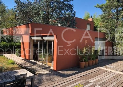Maison moderne avec façade orange et plantes en pot.